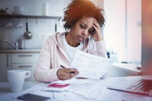 A woman holding a paper and her head looking stressed.